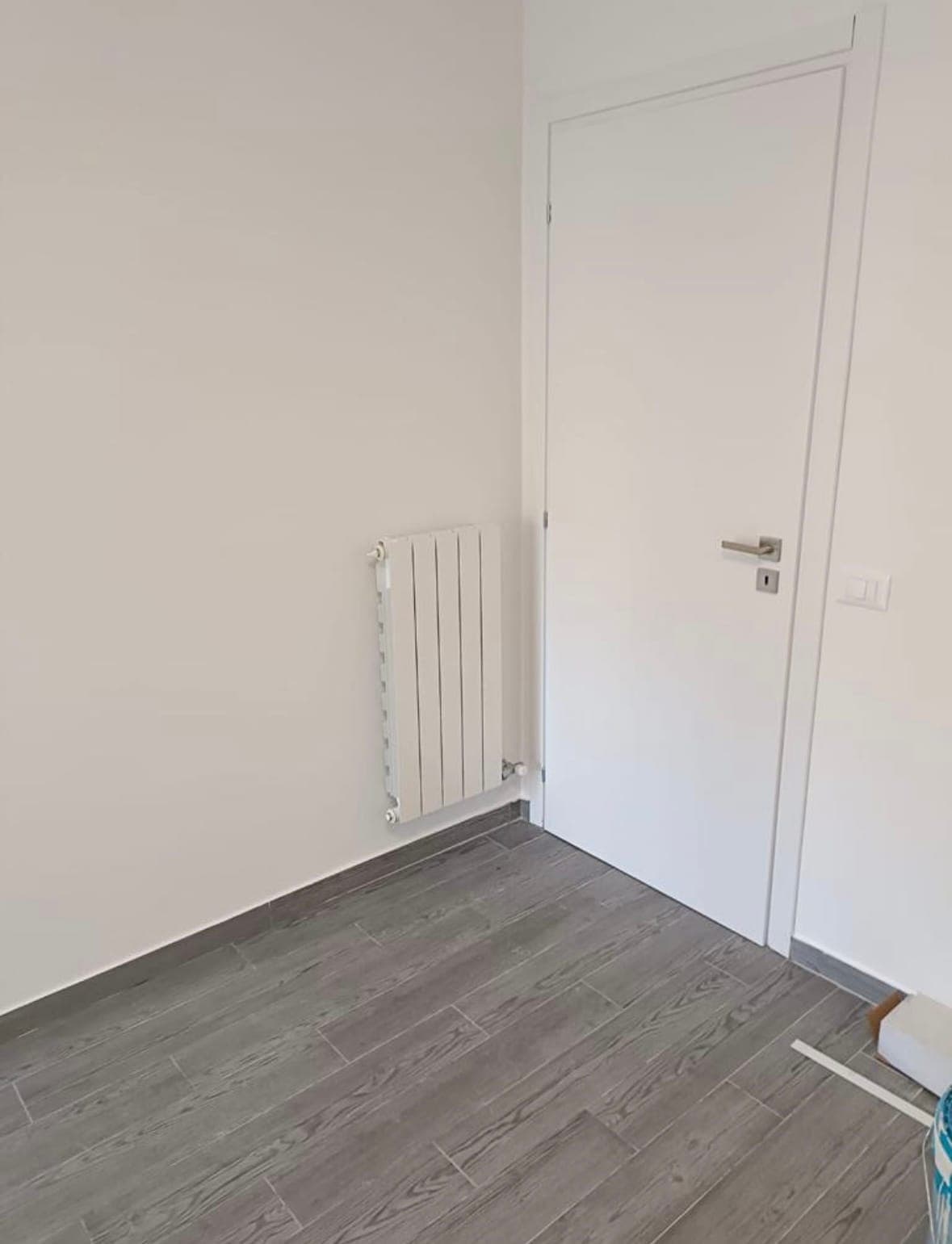 Camera con pareti bianche, porta nuova e pavimento effetto legno
